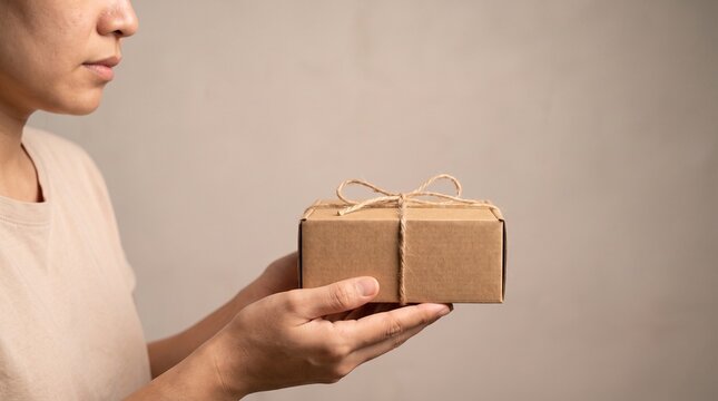 Person holding a small brown cardboard gift box tied with twine, simple packaging for delivery or present