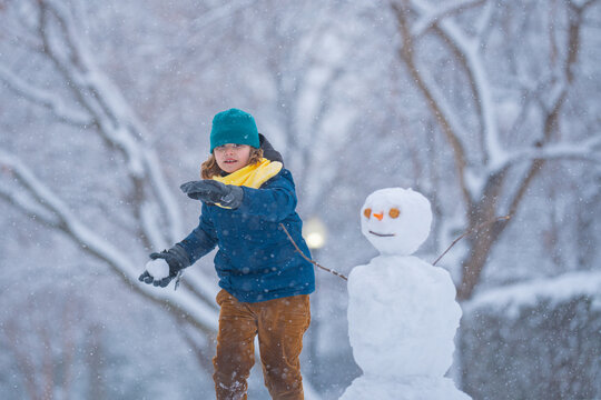 Child throw snowball, winter happiness. Child throwing snowball near a snowman. Child in warm clothes play with snowball during winter. Child smiling in snowball fight . Winter childhood.