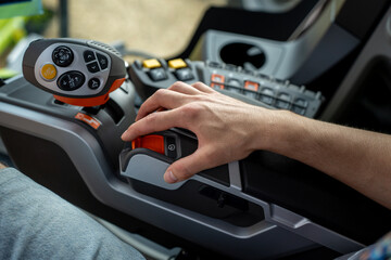 Close-up of an operator's hand using a control lever on a combine harvester cab console, beside a multifunction joystick and buttons. © Marina