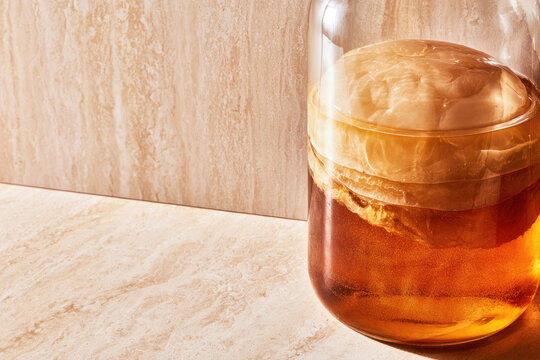 Amber beverage glass jar floating scoby golden liquid travertine surface
