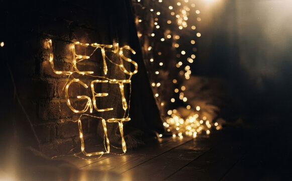 Neon lights spelling Let us get lit against a dark brick wall with fairy lights in the background for party and celebration concept