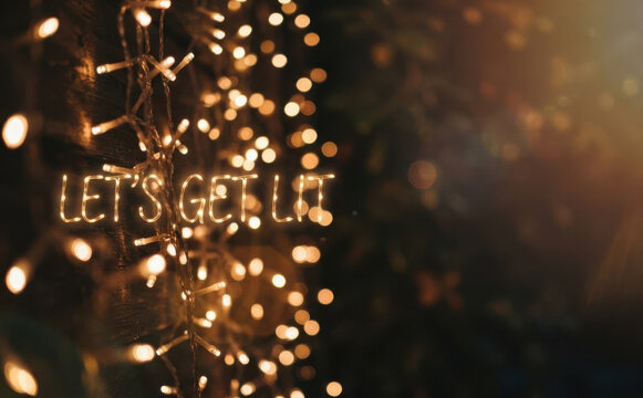 Neon sign spelling lets get lit surrounded by warm glowing fairy lights and bokeh background holiday celebration party decoration