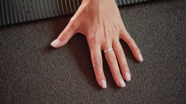 Close up shows adult woman left hand resting flat against dark gray carpet fingers spread naturally. focus remains steady highlighting details of skin texture and simple ring on one finger
