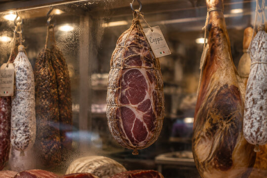 A whole cured coppa salami hanging in a delicatessen display case.