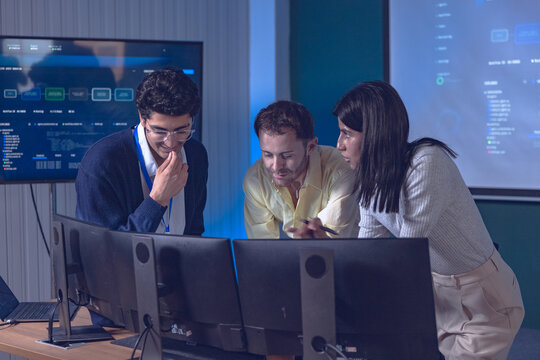 Diverse software team collaborating at computer monitors in a modern office, representing artificial intelligence, AI development, multicultural teamwork, programming, and innovation