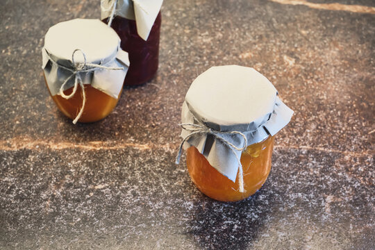 Three jars of fruit jam sealed with paper and string on dark countertop