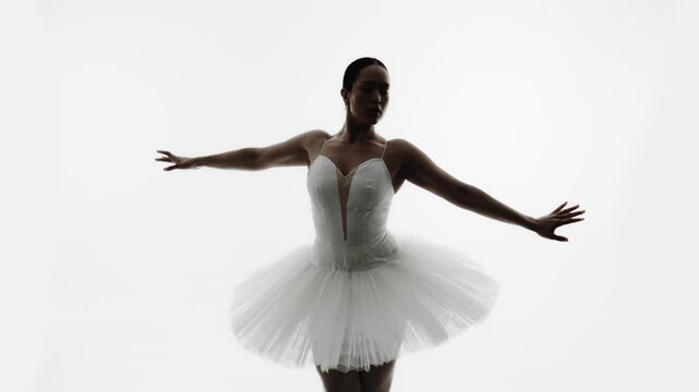 Ballet dancer in white tutu performs graceful classical dance movements in studio