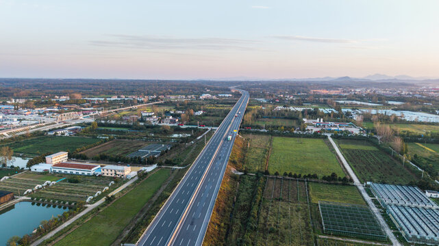 Aerial shot of a multi-lane highway cutting through rural farmland and small settlements under soft light.