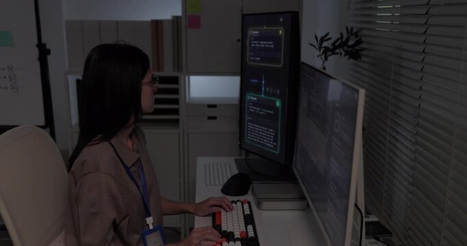 Woman programmer typing on mechanical keyboard with code on dual monitors in software office