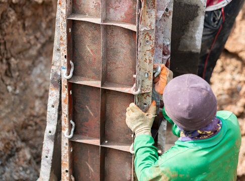 Construction worker wearing protective gloves and work clothing assembling and securing a steel concrete formwork panel at a building construction site.