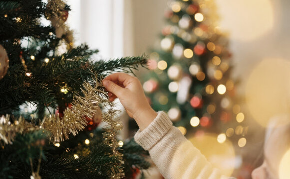 Child decorating Christmas tree with gold tinsel and lights at home during winter holiday