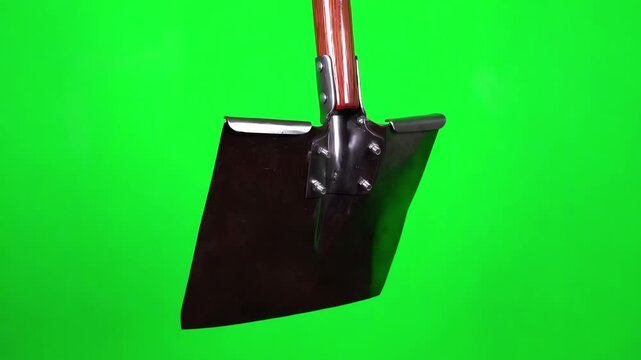 Rotating view of a clean square point shovel with a wooden handle spinning slowly in front of a solid green screen backdrop