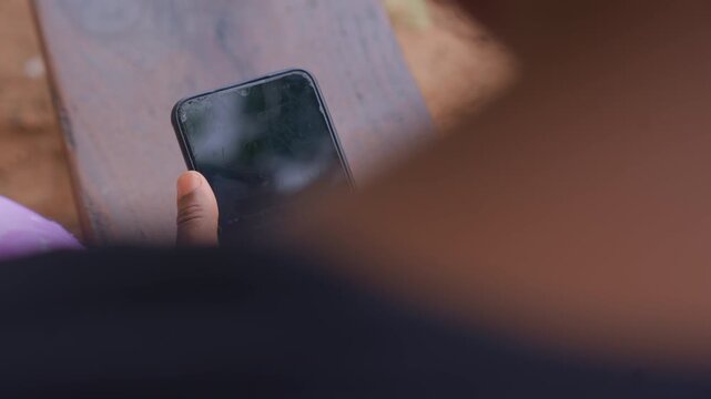Close up shows person arm resting near their body while they hold old cracked smartphone. focus remains consistently on hand and phone with no significant movement or change in setting