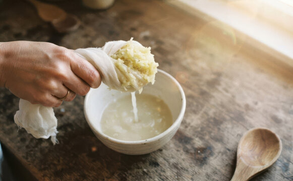 Woman squeezing grated ginger juice in cheesecloth over white bowl for healthy cooking recipe