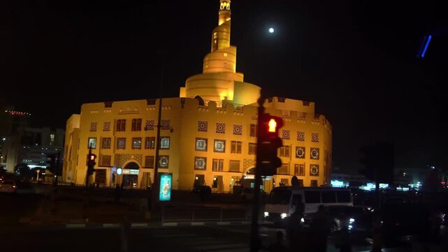 Aerial drone night view of the National Museum of Qatar illuminated against the moon with city traffic and modern architecture in Doha