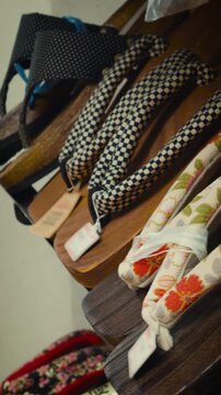 cinematic vertical close-up shot of traditional japanese wooden geta sandals with colorful floral and checkered fabric straps displayed on a shelf