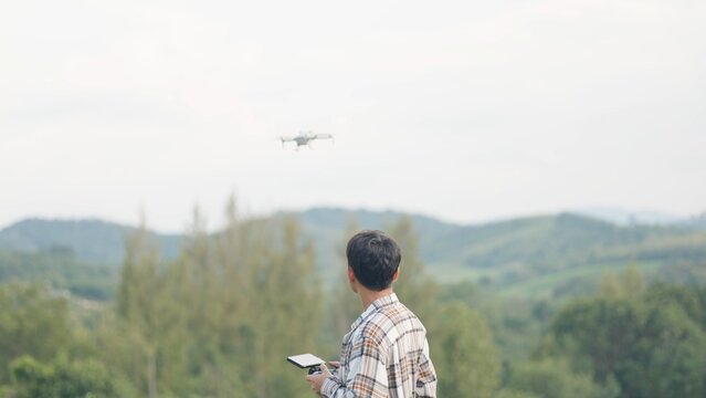 Asian male farmer operating drone with remote controller over green cornfield. Smart agriculture technology, aerial crop monitoring survey and sustainable farming concept.
