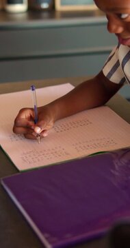 Boy, learning and writing with book in home for mathematics, education or assessment. Child, kid or thinking with notebook, numbers or equations for problem solving, homework or assignment in house
