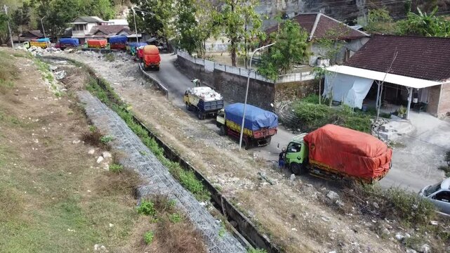 Aerial view of garbage trucks lined up on a narrow road near a waste management site