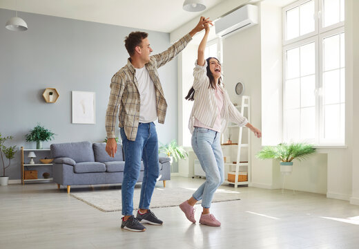 Happy couple dances together at home, enjoying music, love, and fun. They spend leisure time bonding through shared moments, filled with affection in a comfortable and relaxing home atmosphere.