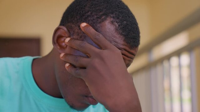 Close up shows thoughtful boy in light blue shirt resting his chin and forehead on one hand indicating deep thought or mild distress. soft indoor lighting highlights subject facial features