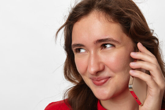 Insider promo deal, young woman with long brown hair talks on smartphone and glances slyly sideways with a cunning smile. Close-up portrait on a light background. Concept of secret deal and insider