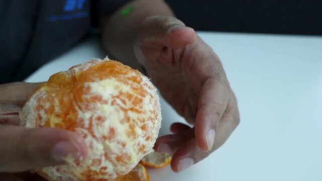 Hands Peeling Fresh Mandarin Orange on White Table