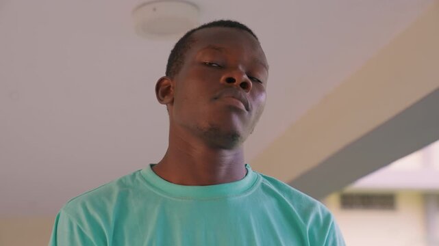 Close up captures upper body and neck of young adult male wearing turquoise t shirt. subject remains stationary positioned indoors with soft lighting against neutral background elements