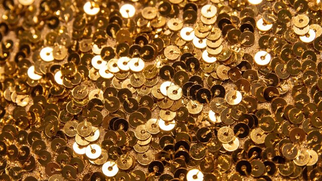 Shiny gold sequin fabric texture with round sequins catching light. Glamorous background for party, fashion or New Year Eve design. Sparkling sequins backdrop