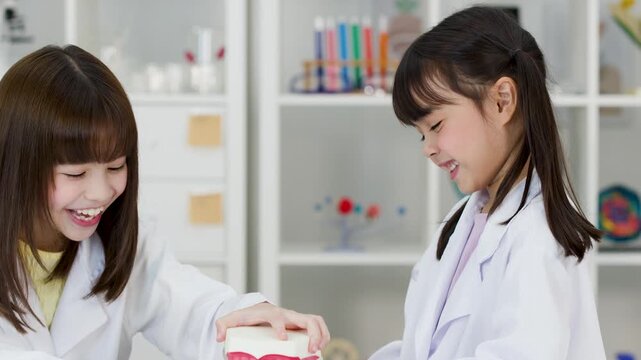 Asian Children in Lab Coats Learning Dental Hygiene with Teeth Model