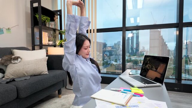 Asian Woman Stretching While Working on Laptop in Modern High-Rise Apartment