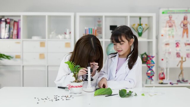 Asian Elementary Students in Lab Coats Using Microscope for Biology Experiment