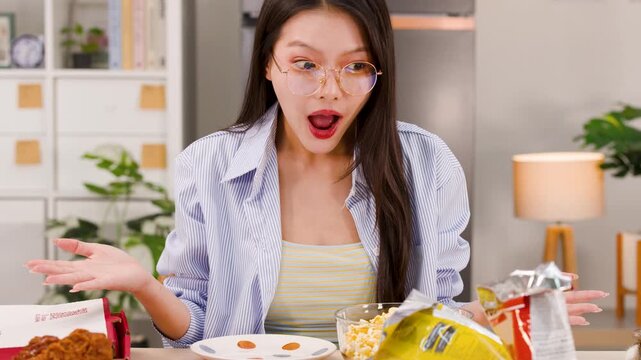 Shocked Asian Woman Expressing Disbelief at Desk Full of Junk Food