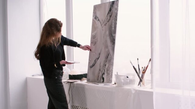 Painter workplace. Abstract art. Woman professional artist using paint palette knife enjoying hobby near window in studio indoor.