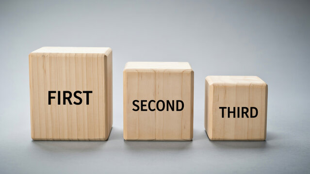 Wooden blocks arranged in descending order labeled first second and third on a neutral gray surface with blocks varying heights heights placed row three wooden labels