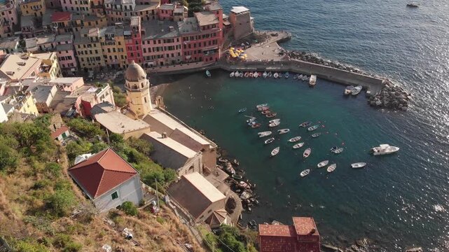 Aerial drone vertical pan rising from the Mediterranean Sea toward Doria Castle in Vernazza, revealing the coastal village and hillside landscape.