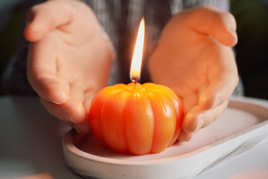 Person enjoying warmth of glowing pumpkin candle at home