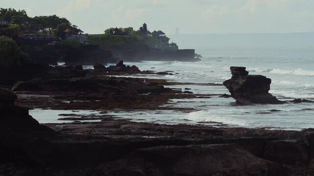 Tanah Lot Temple On Rocky Cliff Dawn, Gentle Waves And Mist Roll Against Sacred Outcrop Cinematic Drone Framing Shows Shrine Silhouette Under Soft Tropical Light, Ideal For Travel, Spiritual place