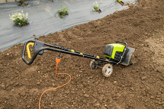 In a residential garden, an electric tiller rests on freshly cultivated dark brown soil in a vibrant garden bed.
