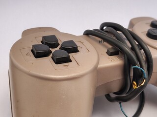 Close-up of a directional pad on a dusty, obsolete retro gamepad with a frayed, broken cable wrapped around its center © Ricko Destu