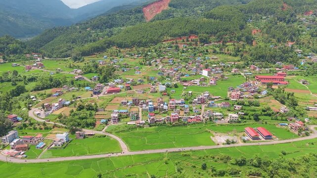 Aerial view of a Nepali town along a flood-scarred river channel filled with thick mud and debris beneath green mountains after a flash flood