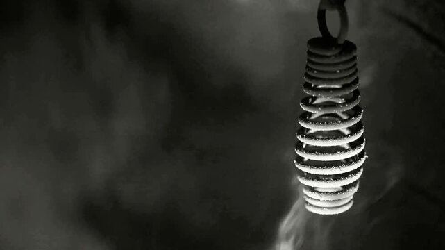 Metal spiral object hanging amidst dense smoke and mist