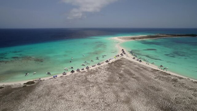 Drone tracks over sandbar with anchored boats and umbrellas in clear tropical water