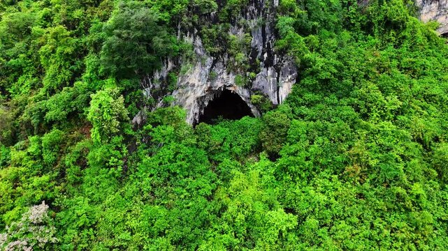 Landscape view: Aerial view of a natural cave surrounded by dense forest in a karst mountain landscape.