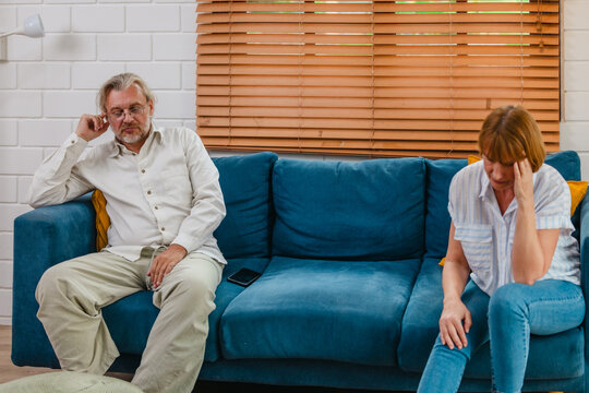 Upset senior couple sitting apart on sofa after argument at home