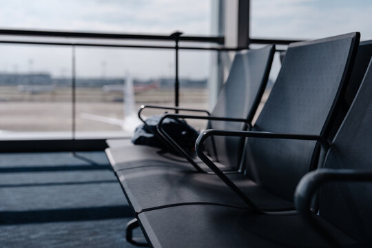 Empty passenger seats in a modern airport waiting area with large windows overlooking the runway.