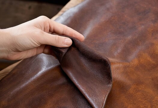 Close-up of a hand gently holding and folding rich brown leather material