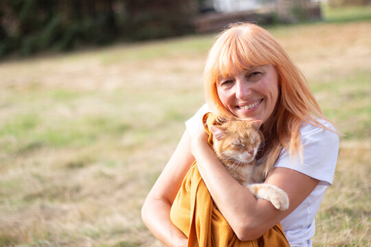 Smiling Blonde Woman Holding Adorable Orange Cat During Outdoor Picnic in Park