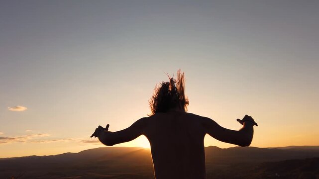 Slow motion rear view of shirtless man with long hair dancing at sunset on a mountain ridge