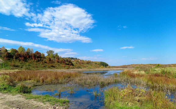 Autumn rural landscape with swampy meadow and blue sky.